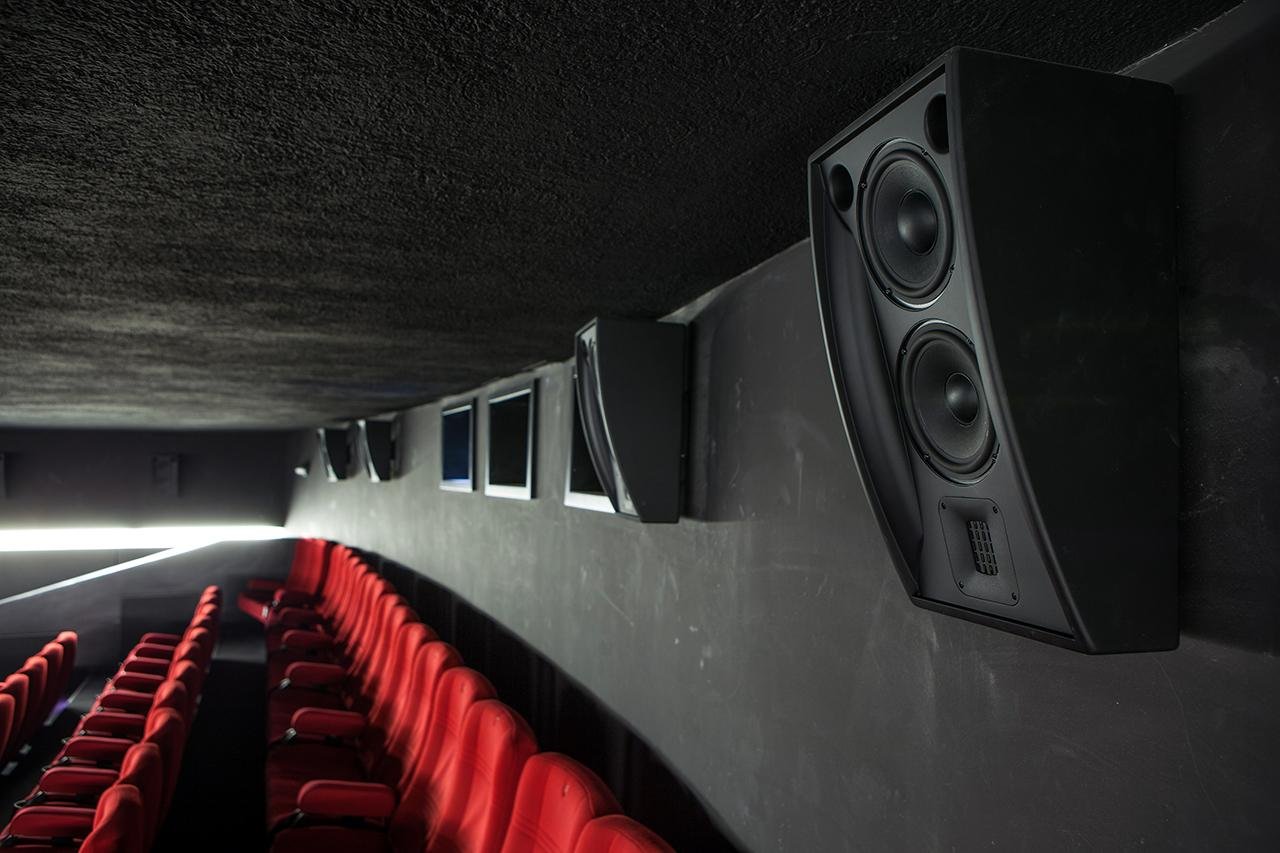 Sala de cinema com alto-falantes nas paredes e tela de projeção